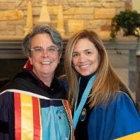 Two faculty members posing for a photo in their academic regalia.